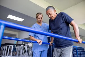 Latin American man doing physical therapy and walking holding handbars and guided by a physical therapist