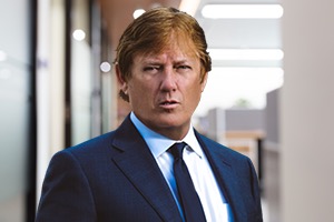 Headshot of Attorney Rusty Galloway wearing a navy suit with blurred office in background.