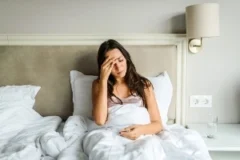 A woman sitting in a bed with a headache.
